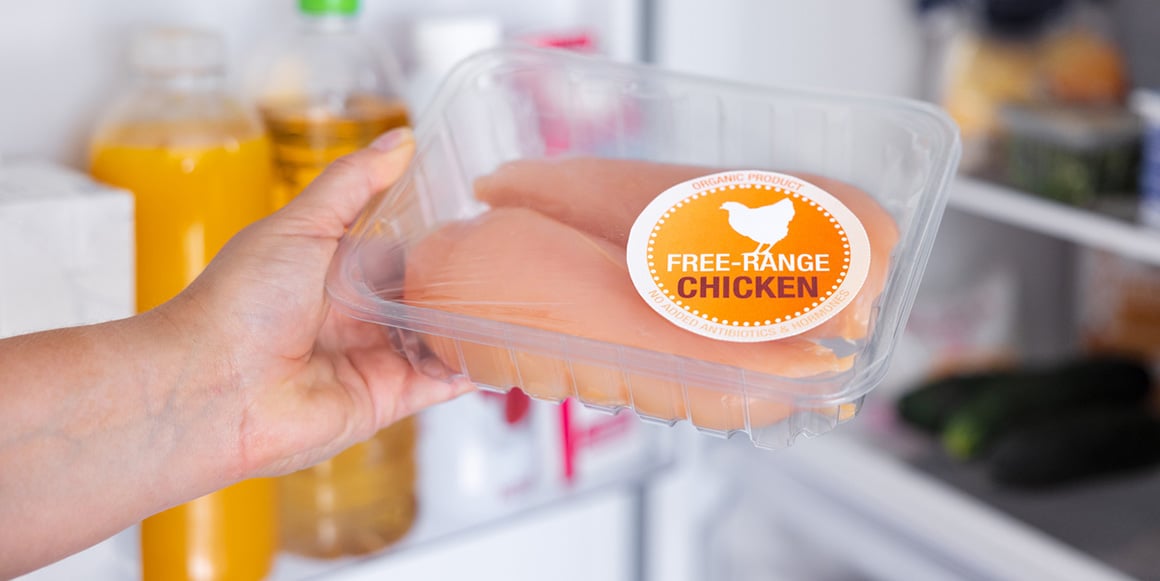 Buyer selecting free-range chicken with a custom food label from a refrigerator shelf